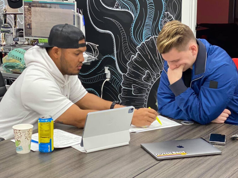 Jason Barker and Nik Madison, members of Custom Fit Real Estate Group, working together in the Custom Fit Real Estate office discussing buying and selling homes in Las Vegas, Nevada.